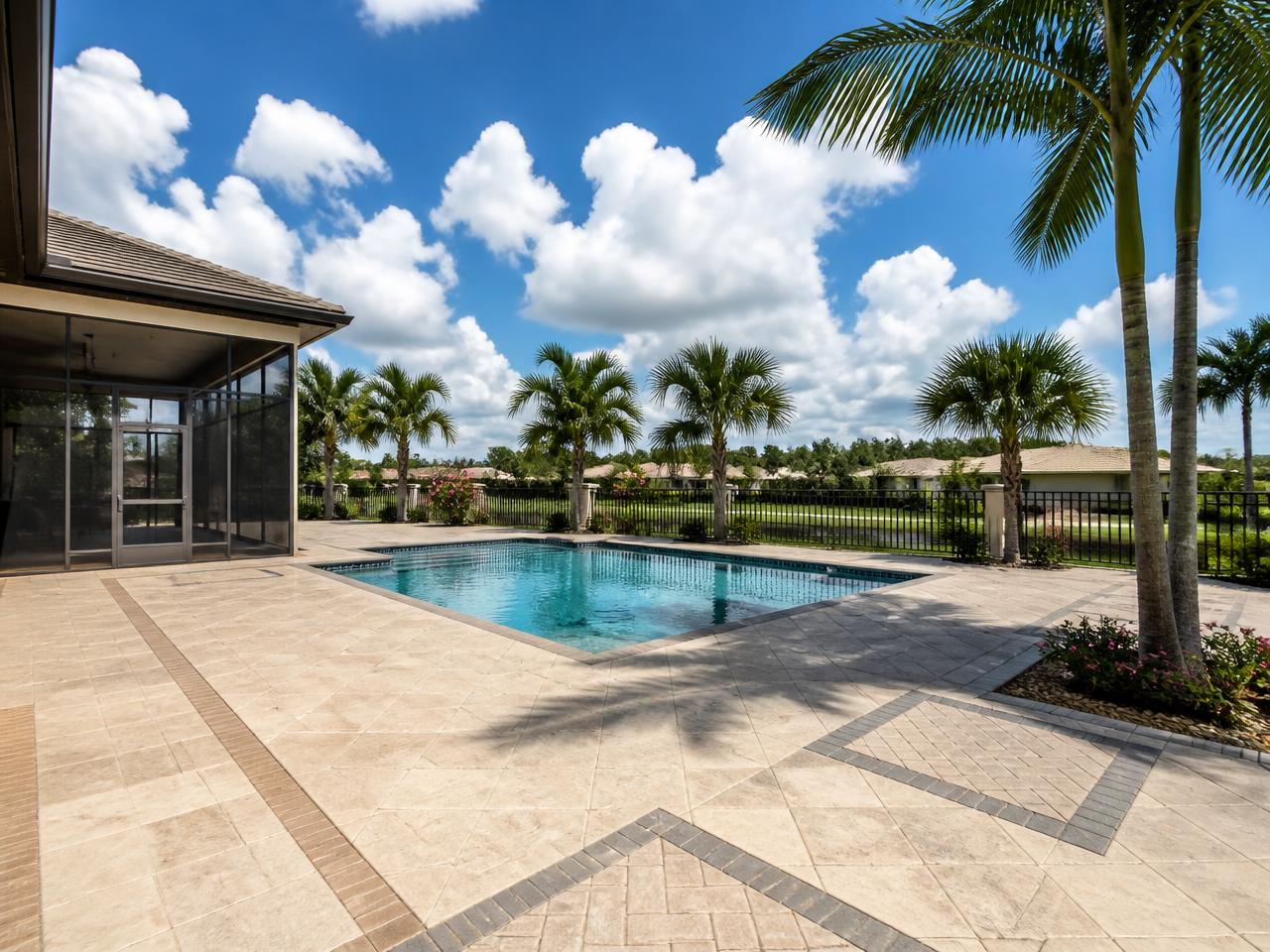 Paver pool deck with outdoor kitchen and lounging area under bright midday sun
